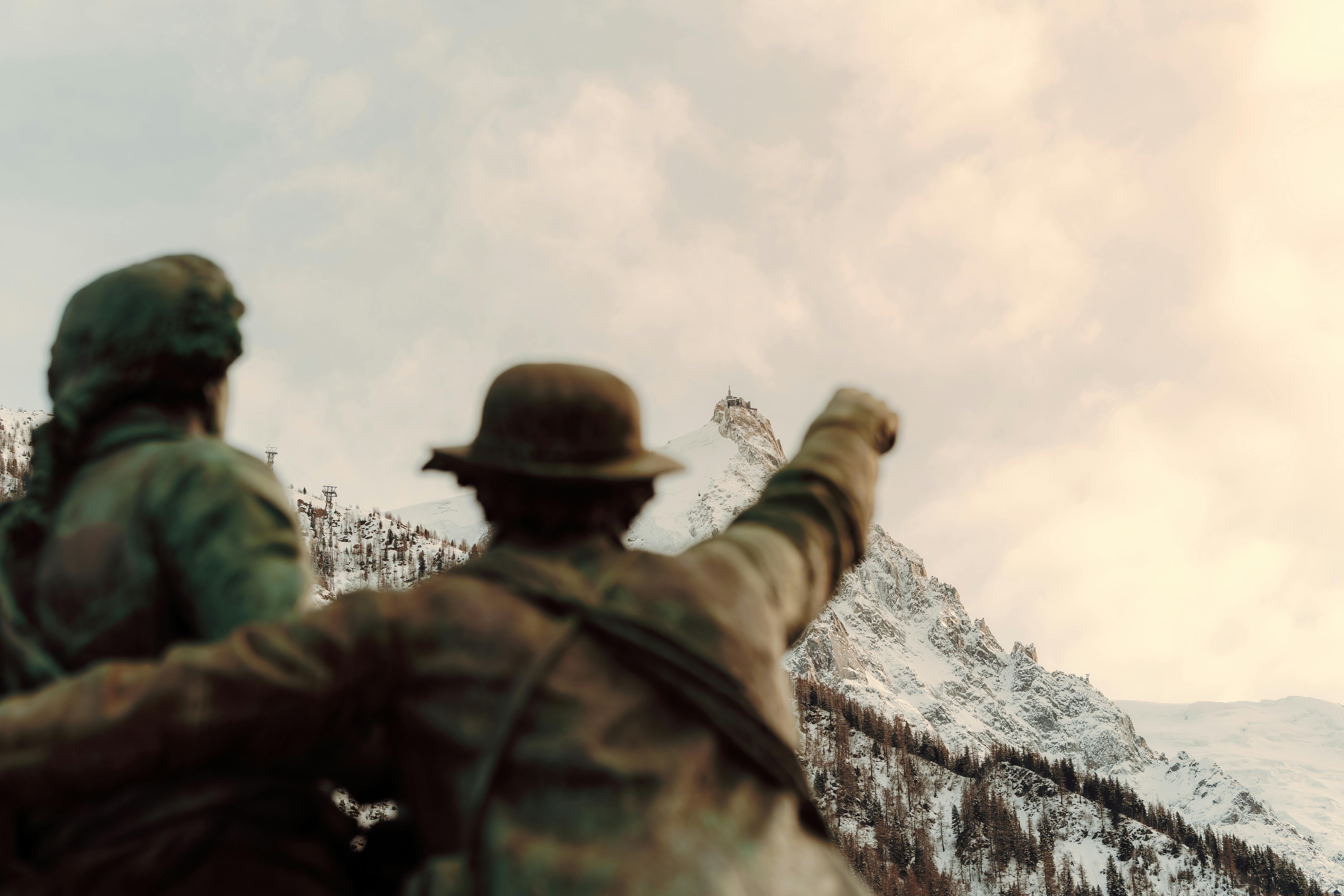 ingyenes Bronzszobor, amely egy hófödte hegycsúcs felé mutat, drámai, felhős égbolttal. Stockfotó