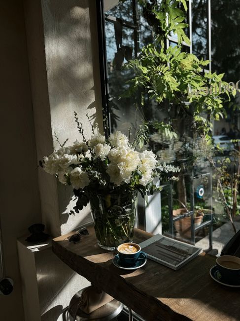 Sunlight bathes a café's floral arrangement and coffee, creating a serene atmosphere.