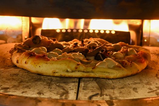 Golden-brown pizza baking in a traditional wood-fired oven, melting cheese and crackling crust produce inviting aroma.