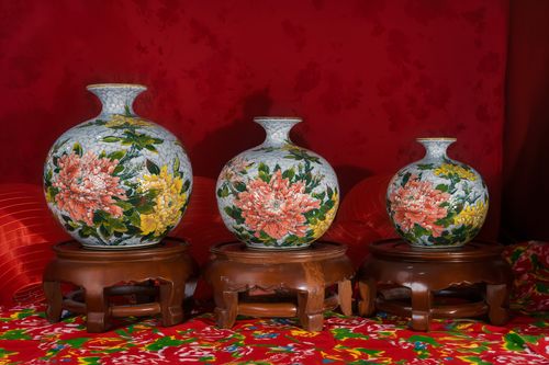 Free Trio of artistic vases with colorful floral patterns on wooden stands, set against a rich red background. Stock Photo