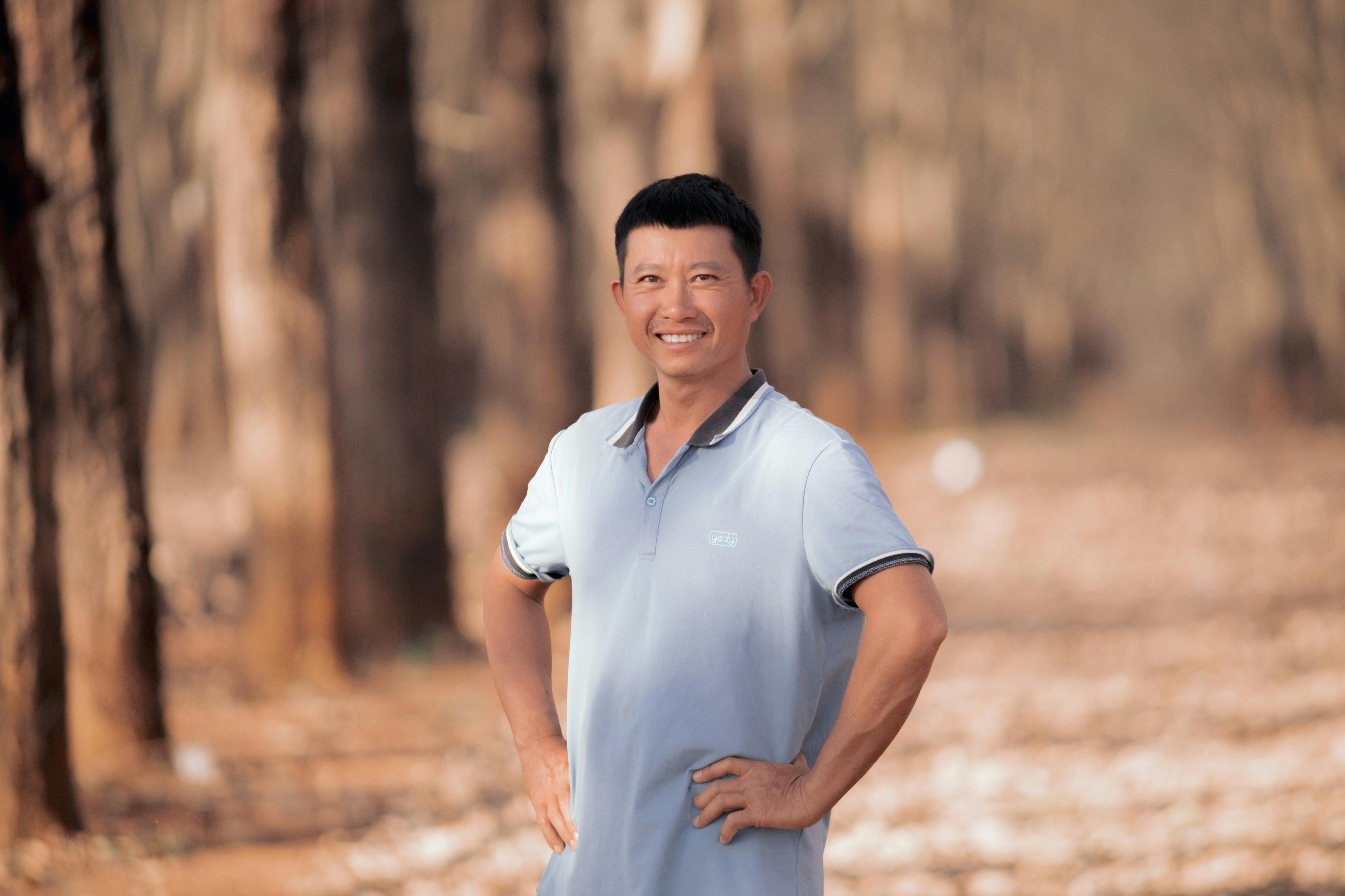 A cheerful man standing among rubber trees in Kon Tum, Vietnam.