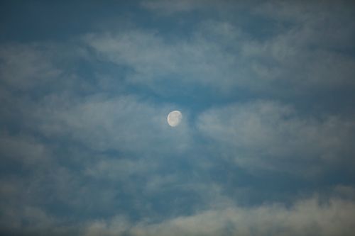 Free A mesmerizing view of the half moon surrounded by clouds during twilight, set against a serene blue sky. Stock Photo