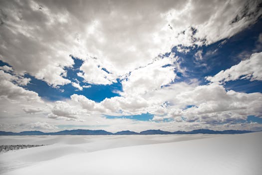 Wide view of White Sands National Monument with dramatic cloudscape and mountains in the distance.