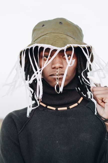 Close-up portrait of a fashionable young man wearing a unique hat and accessories.