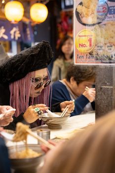 Street scene of people enjoying noodles at a bustling izakaya in Shinjuku, Tokyo.