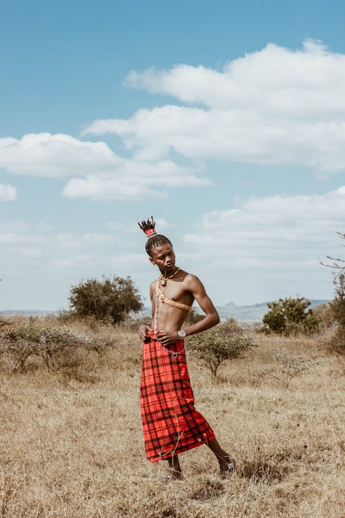 Man in Red and Black Checkered Skirt Standing on Dry Grass Field