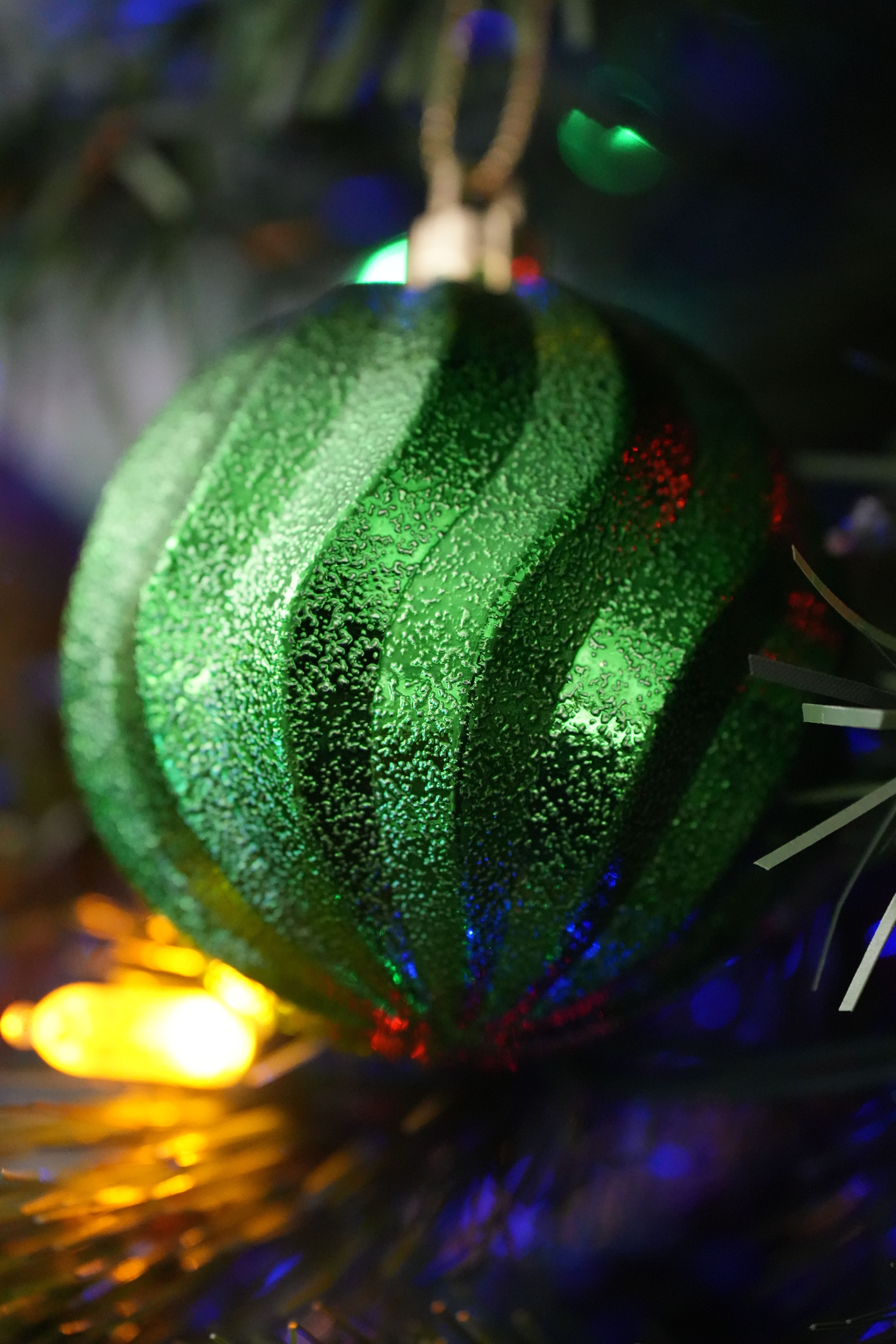 Close-up of a green Christmas ornament with lights on a tree branch.