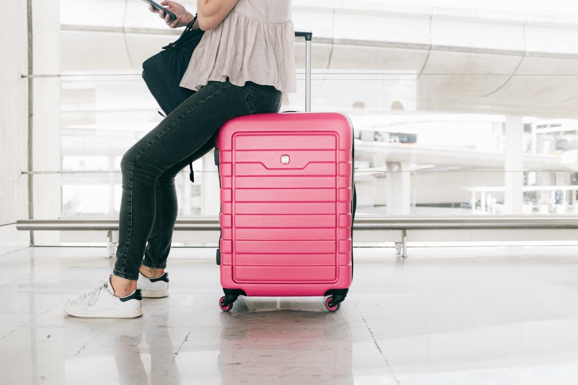 Free Woman In White Top And Denim Jeans Sitting  On Red Luggage Bag Stock Photo