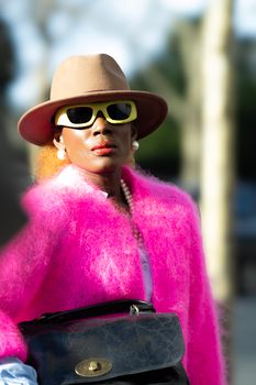 Elegant woman in pink outfit with hat and sunglasses exuding fashion and style outdoors.