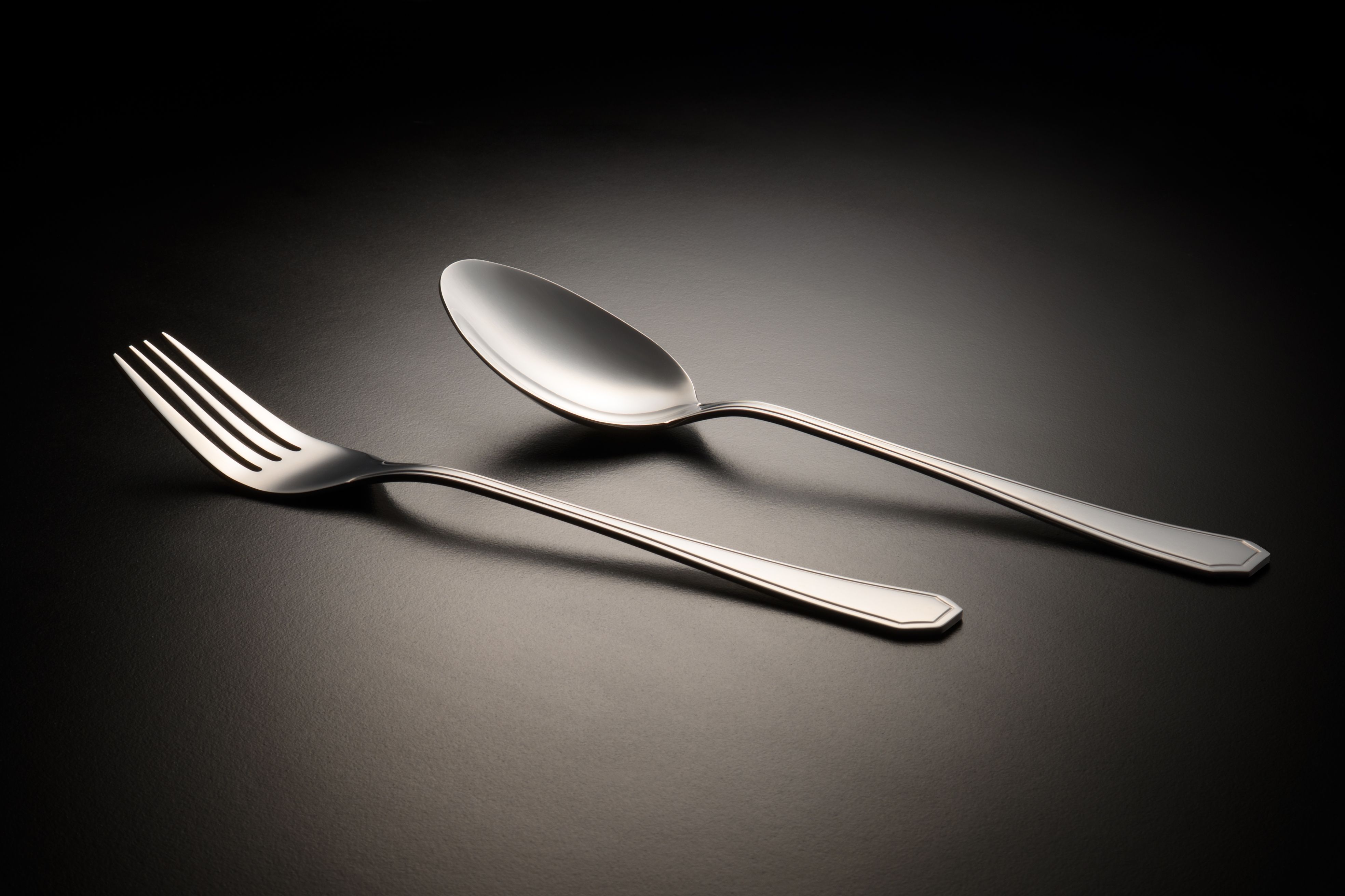 Sleek stainless steel fork and spoon on a black surface, minimalist elegance.