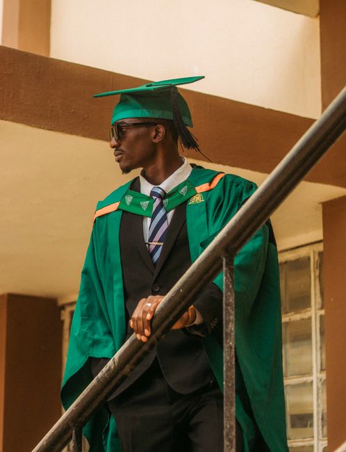 Confident young graduate in green cap and gown standing on staircase with sunglasses. Confident young graduate in green cap and gown standing on staircase with sunglasses.