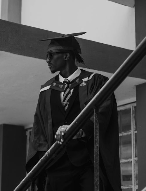 Free Elegant black and white photo of a graduate in traditional cap and gown attire standing on stairs. Stock Photo