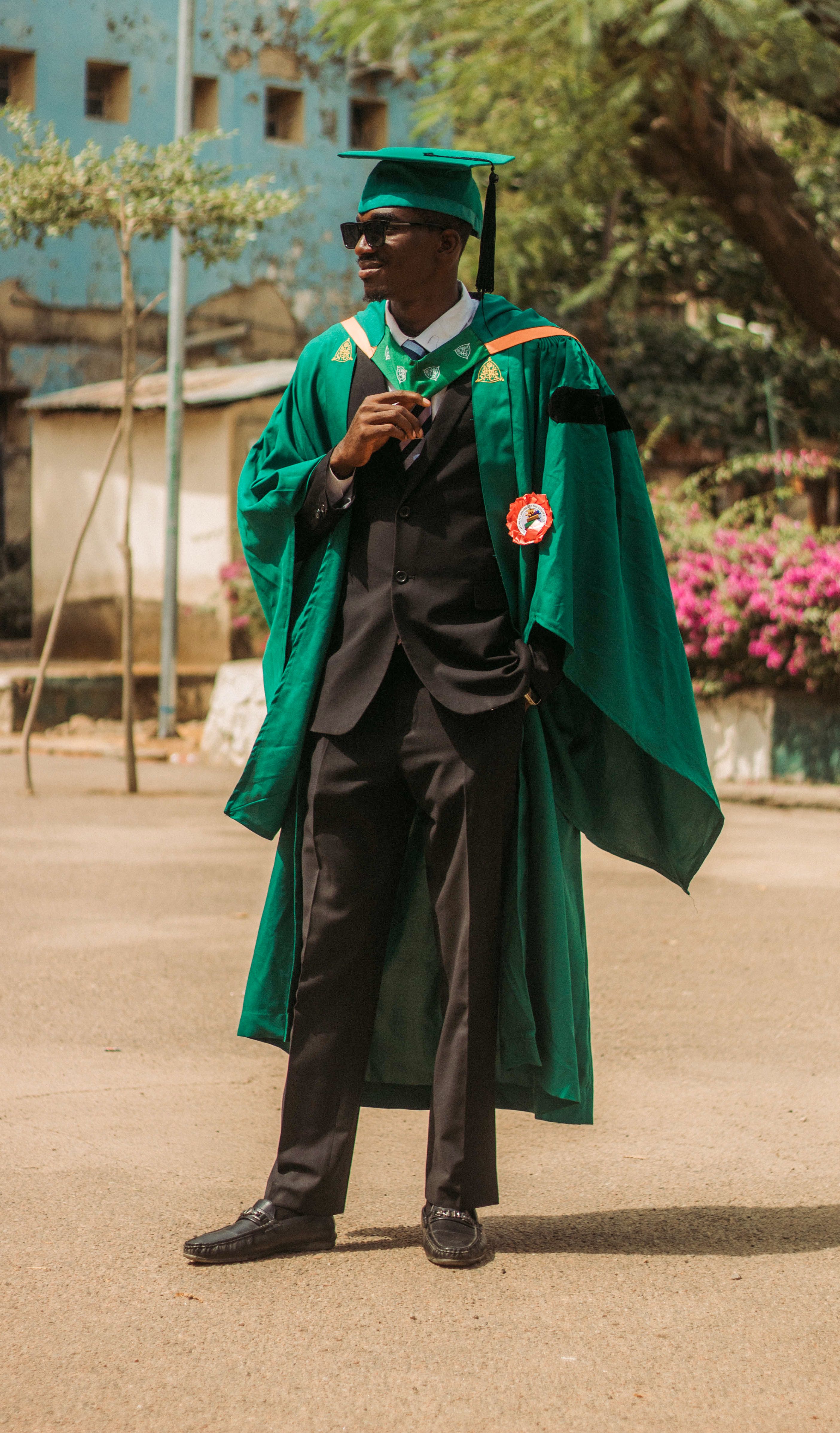 Graduate wearing green gown and cap at outdoor ceremony.