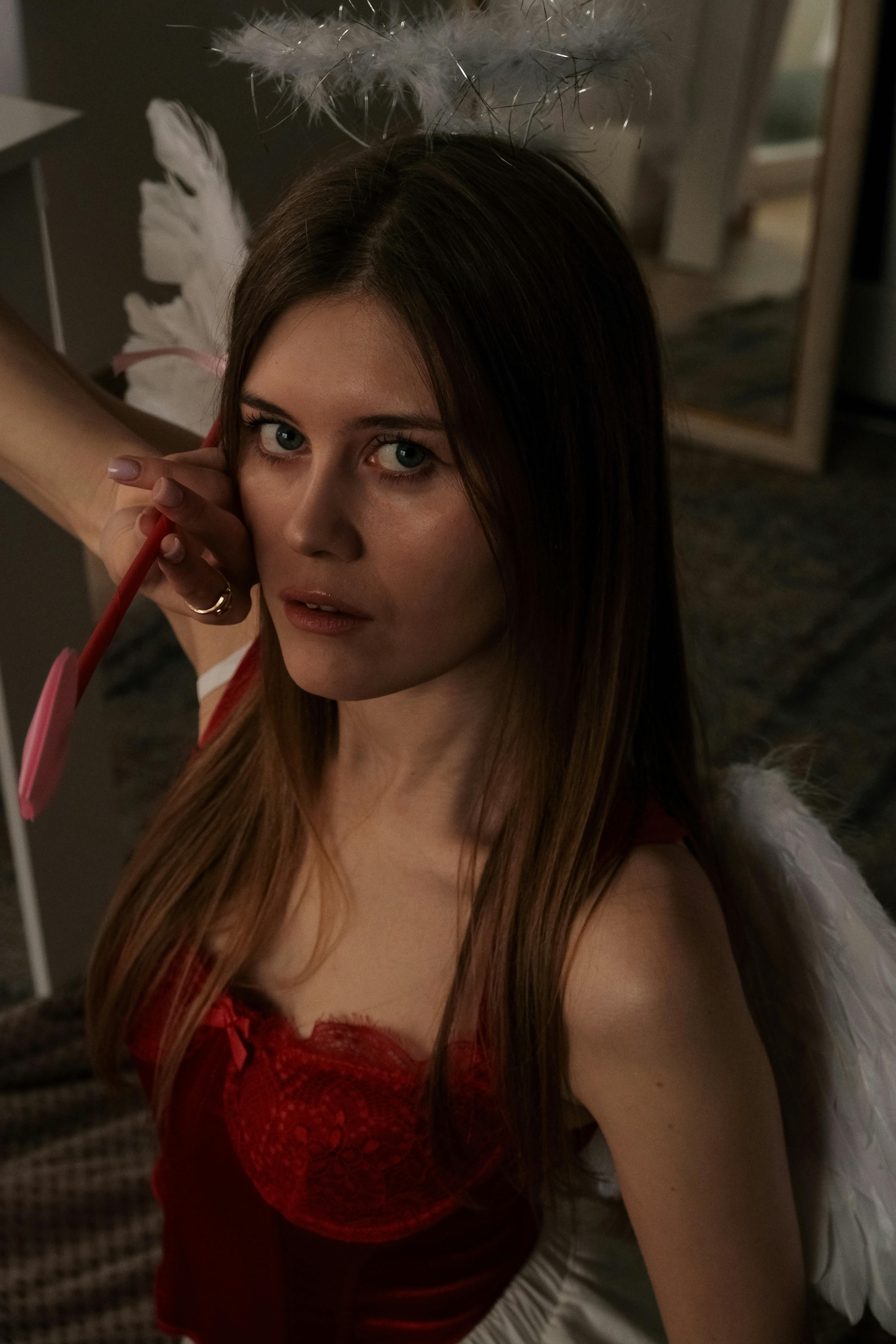 grátis Uma mulher de vestido vermelho e asas de anjo posa no interior, personificando um tema angelical e fantasioso. Foto profissional