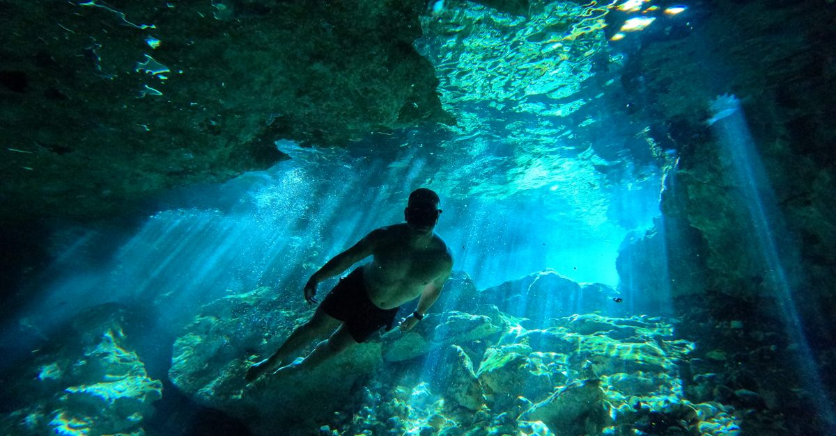 Diver explores a mesmerizing underwater cave with sunlight streaming through.