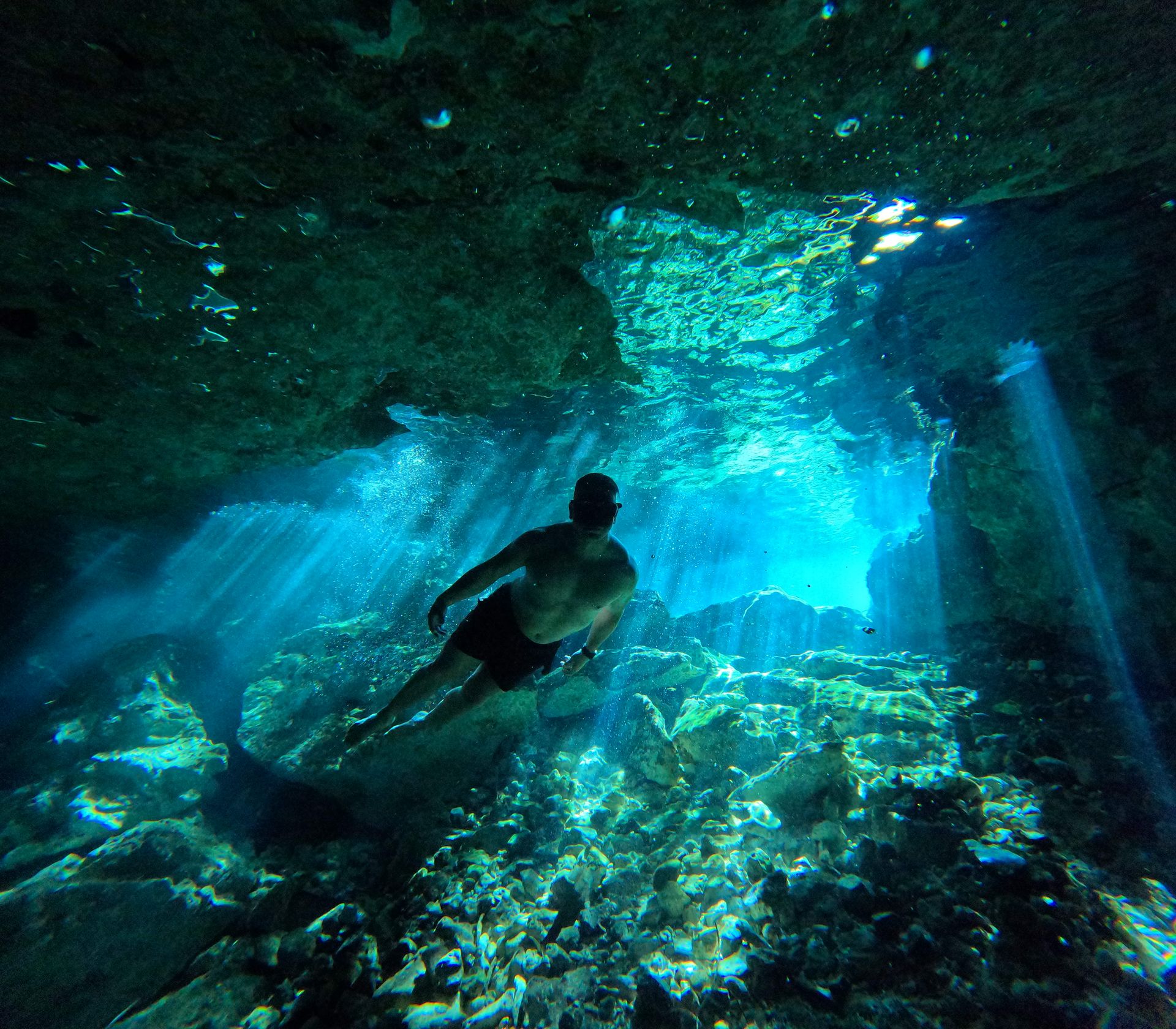 Diver explores a mesmerizing underwater cave with sunlight streaming through.