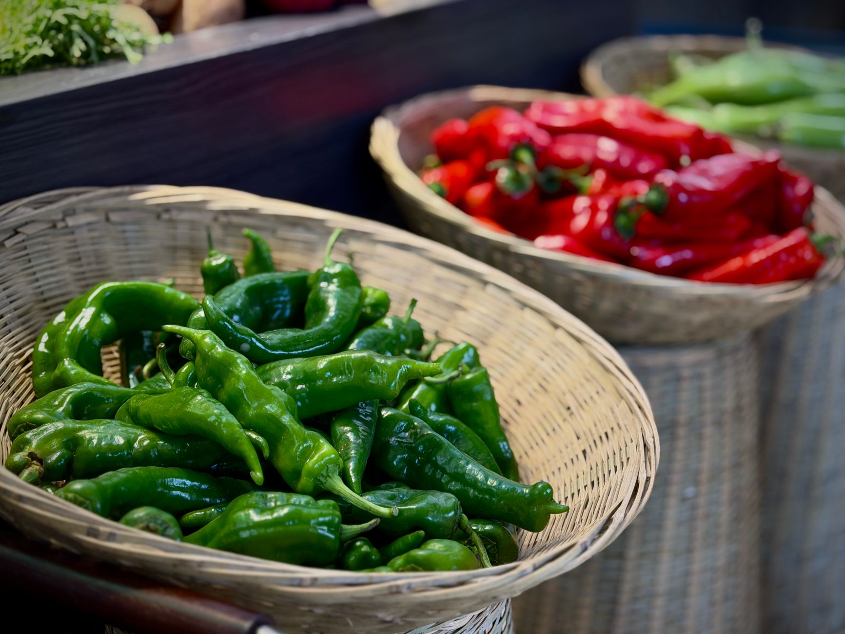 Close-up of fresh red and green peppers in woven baskets at a local market.
