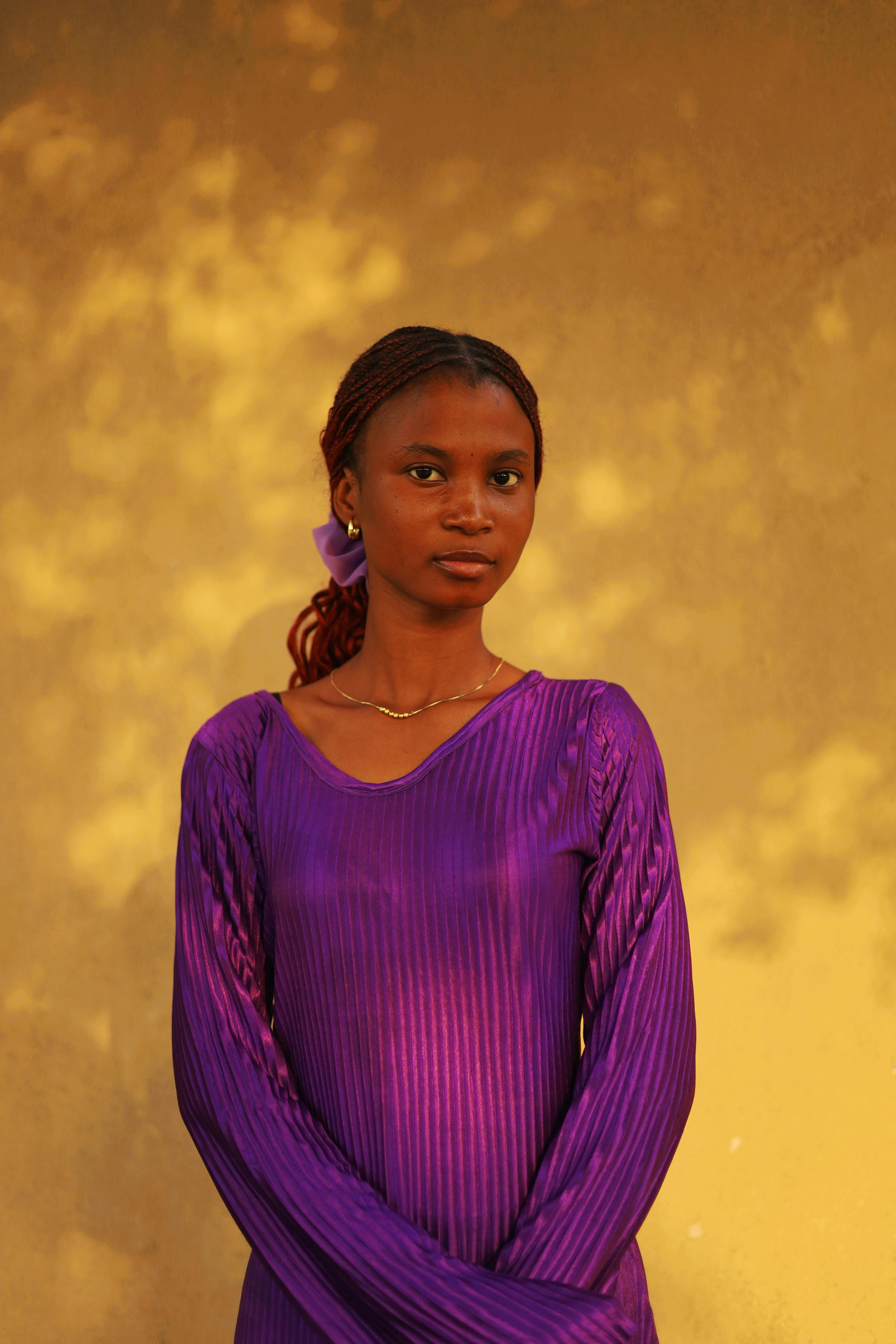 Gratis Portrett av en kvinne i et lilla antrekk, stående mot en varm, teksturert vegg, som fanger essensen av ynde. Arkivbilde