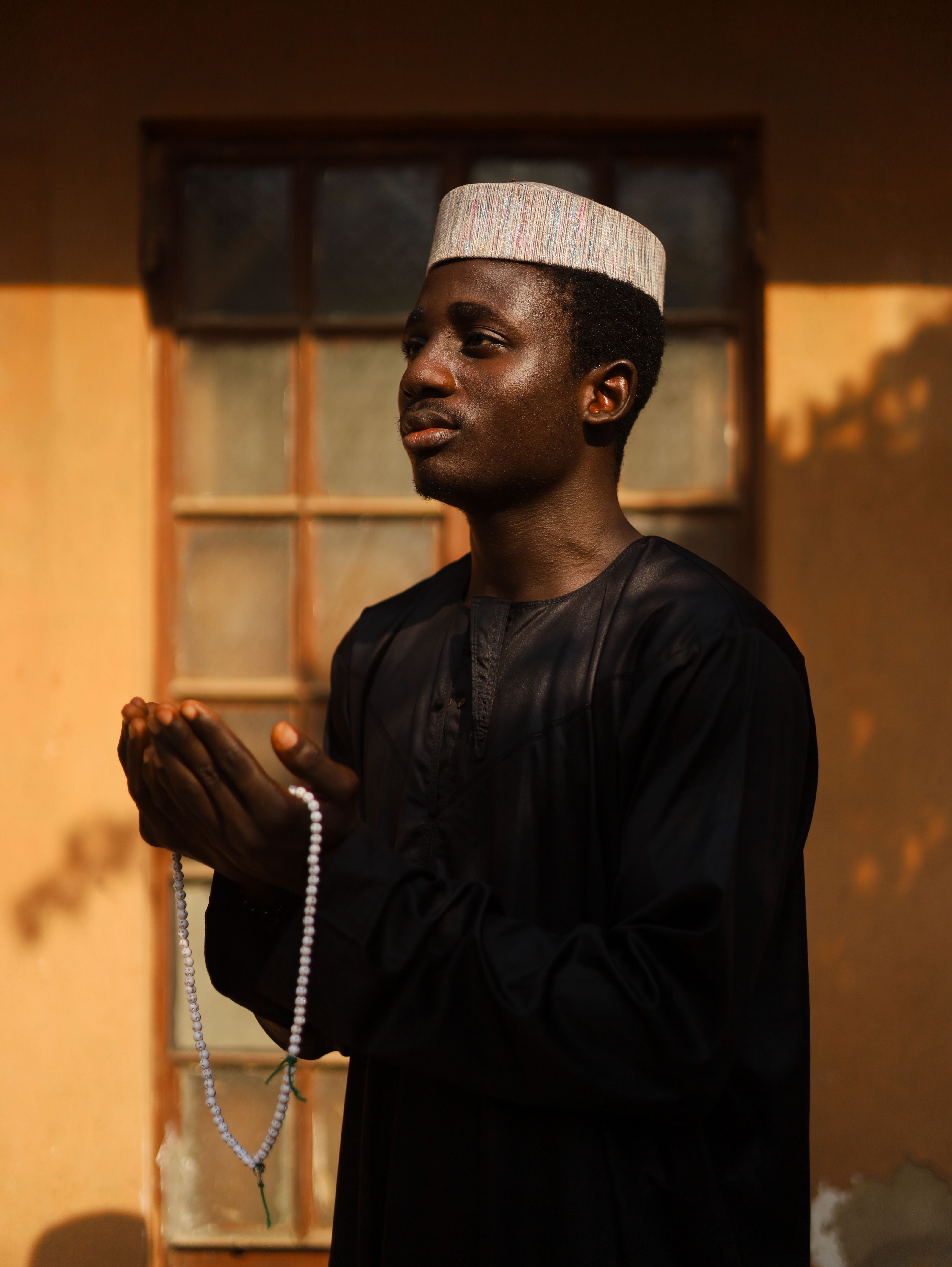 A man in traditional attire prays with tasbih beads outside in natural light.