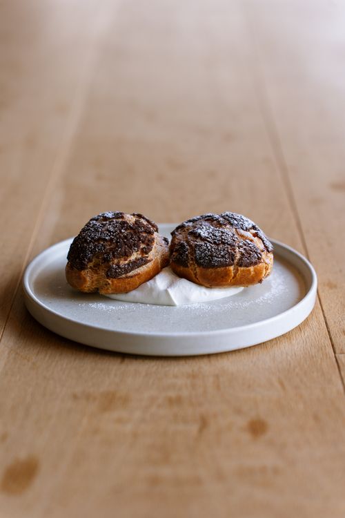 Free Delicious chocolate cream puffs dusted with sugar on a plate, perfect for bakery or dessert themes. Stock Photo