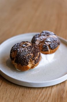 Delicious chocolate-topped cream puffs dusted with sugar on a minimalist plate in a Tokyo cafe.
