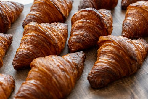 Free Close-up of golden, flaky croissants freshly baked and displayed on a wooden surface. Stock Photo