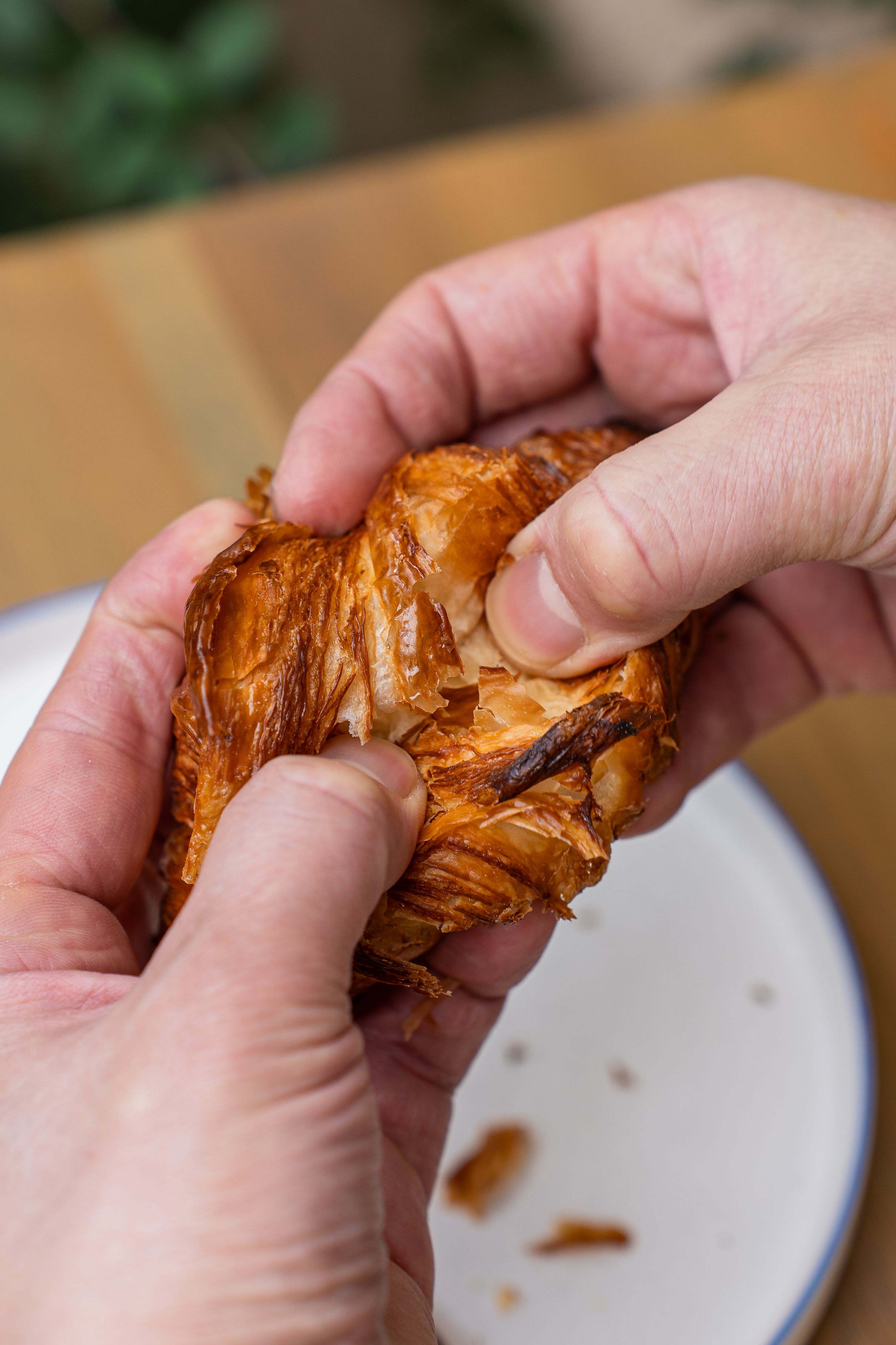 Hands tearing a flaky croissant on a plate in a café. Perfect for food and culinary themes.