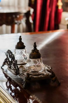 Vintage inkwell set on elegant desk with rich drapery in background.