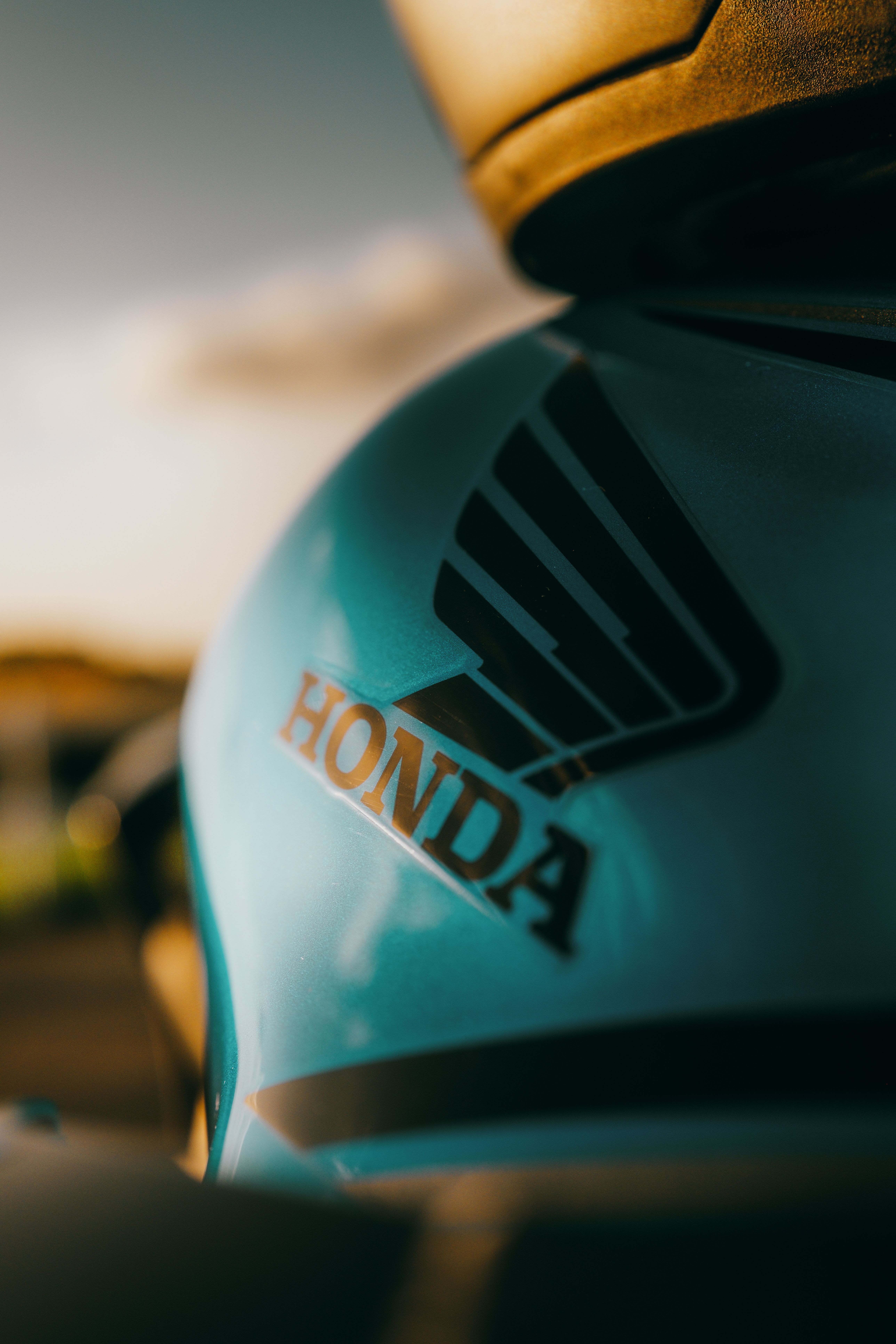 Artistic close-up of a Honda logo on a motorcycle tank during a sunny day.