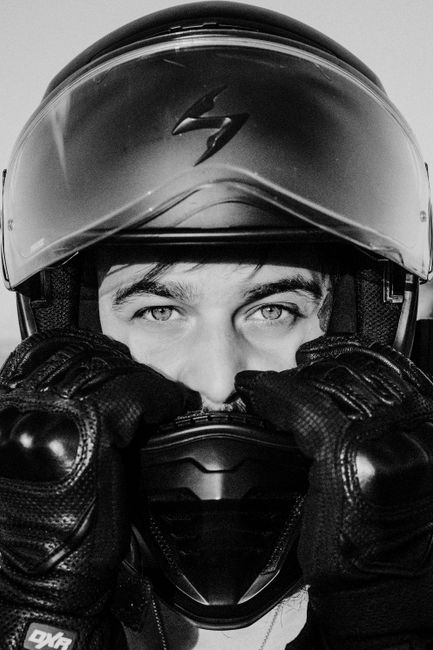 Black and white image of a motorcyclist wearing a helmet and gloves, with a focused gaze.
