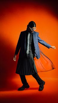 Stylish man in modern attire with an orange background, showcasing unique fashion sense.