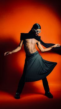 A stylish male dancer in a dynamic pose, wearing black attire against a vivid orange background, exuding modern fashion.