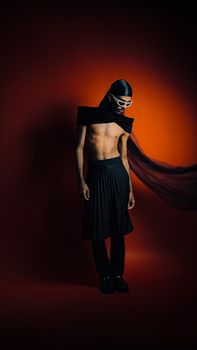 Bold fashion portrait of a man in a dynamic black outfit against an orange backdrop.