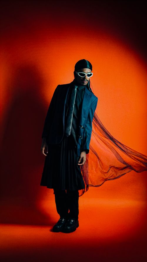 Free Stylish individual in trendy attire poses against a vibrant orange backdrop. Stock Photo