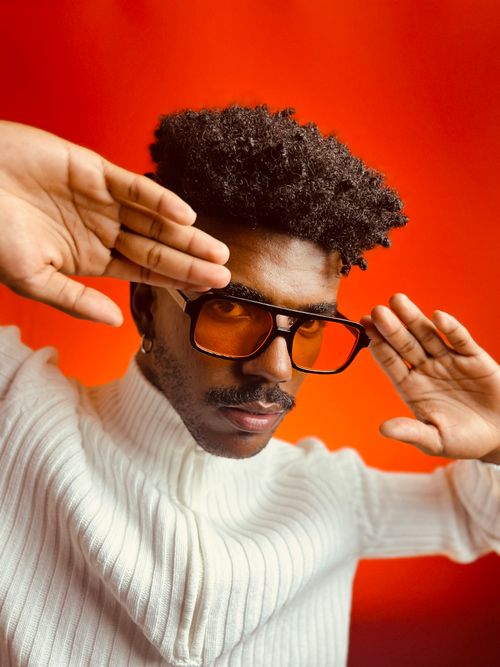 Free A modern portrait of a man wearing sunglasses and a turtleneck, posing against a vibrant red background. Stock Photo