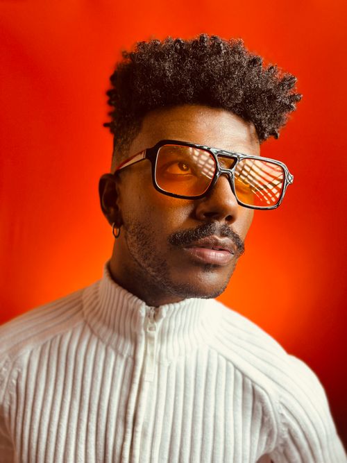 Free Fashionable man wearing sunglasses poses against a vibrant orange background. Stock Photo
