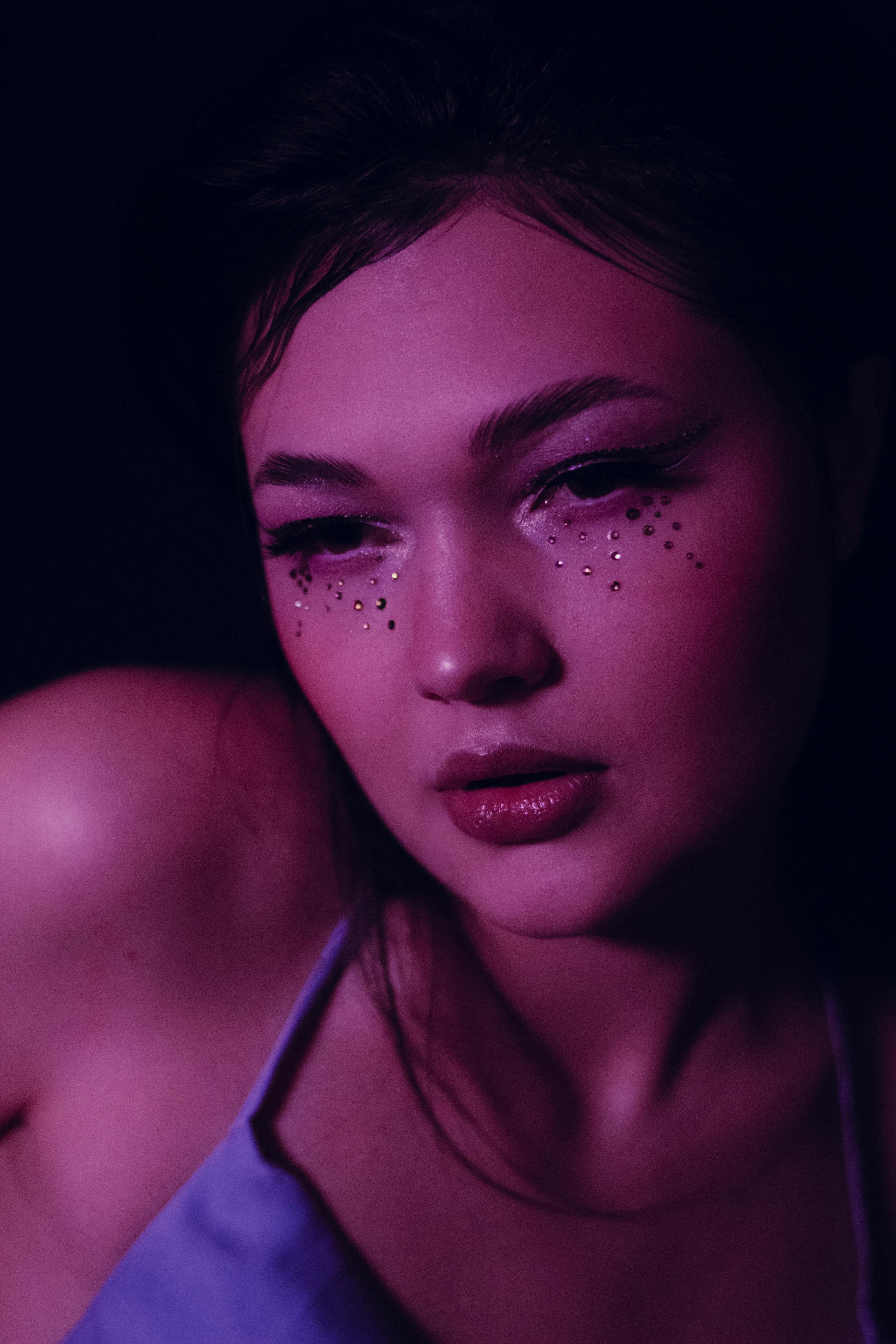 grátis Um retrato melancólico de uma mulher com maquiagem brilhante sob iluminação rosa e roxa. Foto profissional