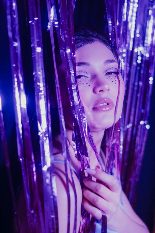 Free A striking portrait of a woman surrounded by glittering purple streamers under vibrant lighting. Stock Photo