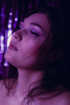 A creative portrait of a woman with glittery eye makeup against a purple backdrop.