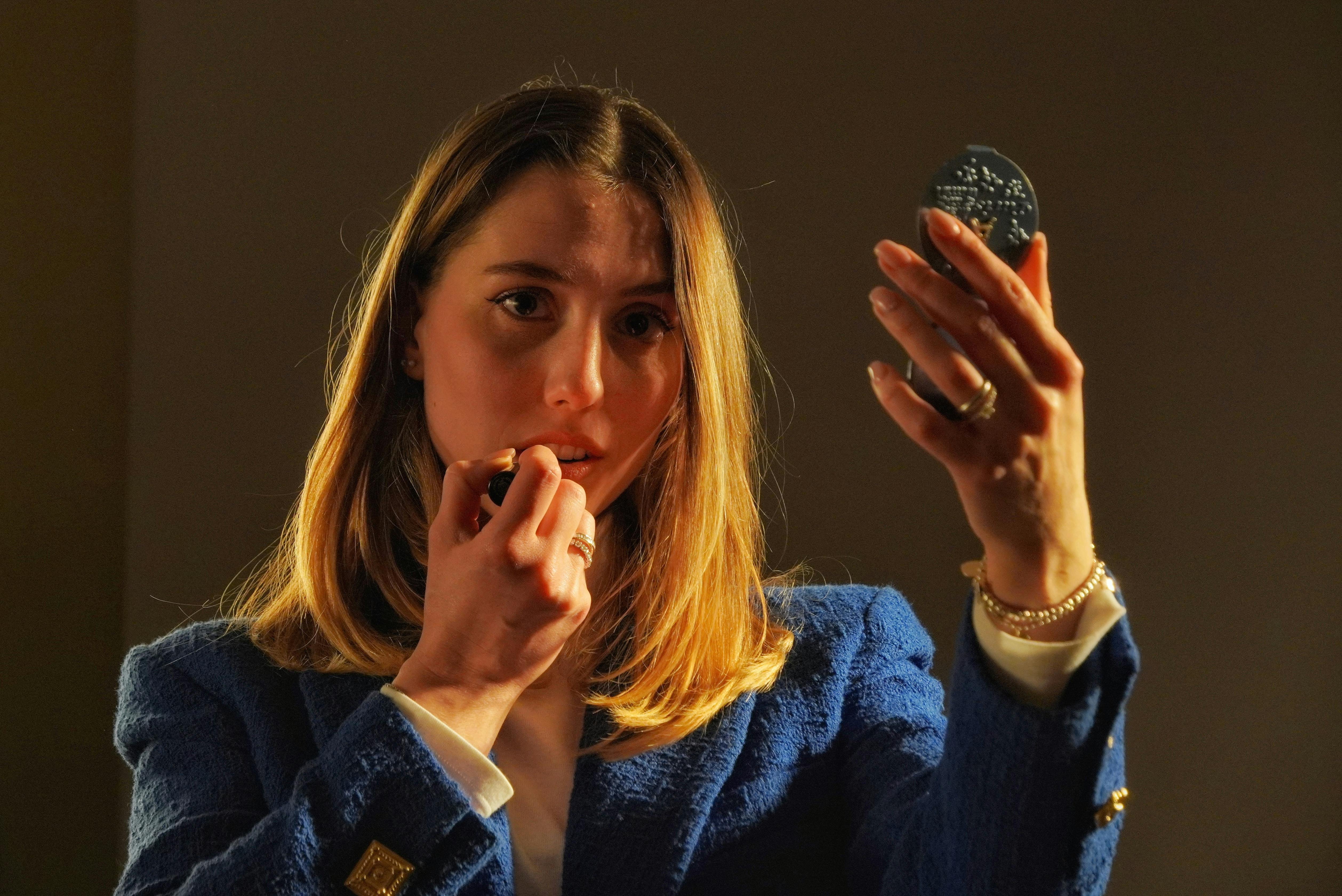 ingyenes Nő rúzst ken, miközben egy kompakt tükröt tart a kezében egy melegen megvilágított környezetben. Stockfotó