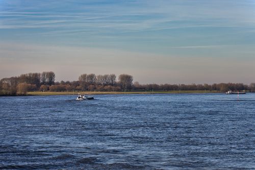 Free A cargo ship navigates a tranquil river with a serene landscape and blue sky, perfect for travel and transport themes. Stock Photo