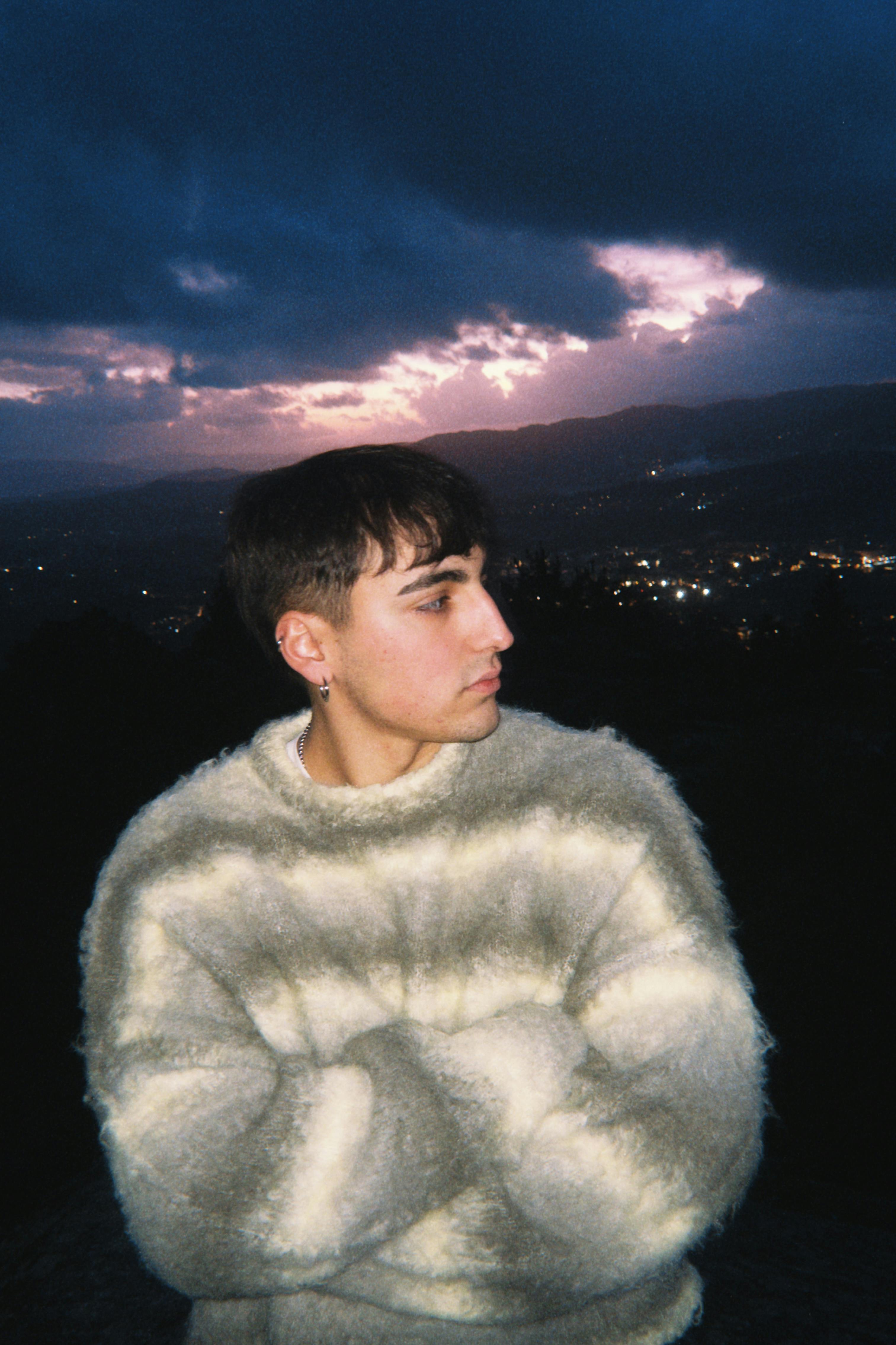 Portrait of a young man in a fluffy sweater with a dramatic sunset background.