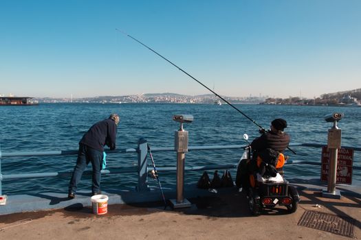 Men fishing by the Bosphorus in Istanbul, with a view of the city and Bosphorus Bridge.