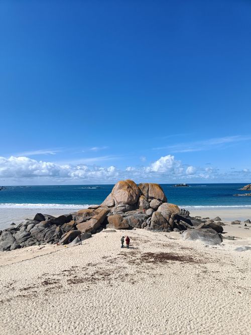 Free Beautiful beach with two people near large rocks under a clear blue sky. Stock Photo