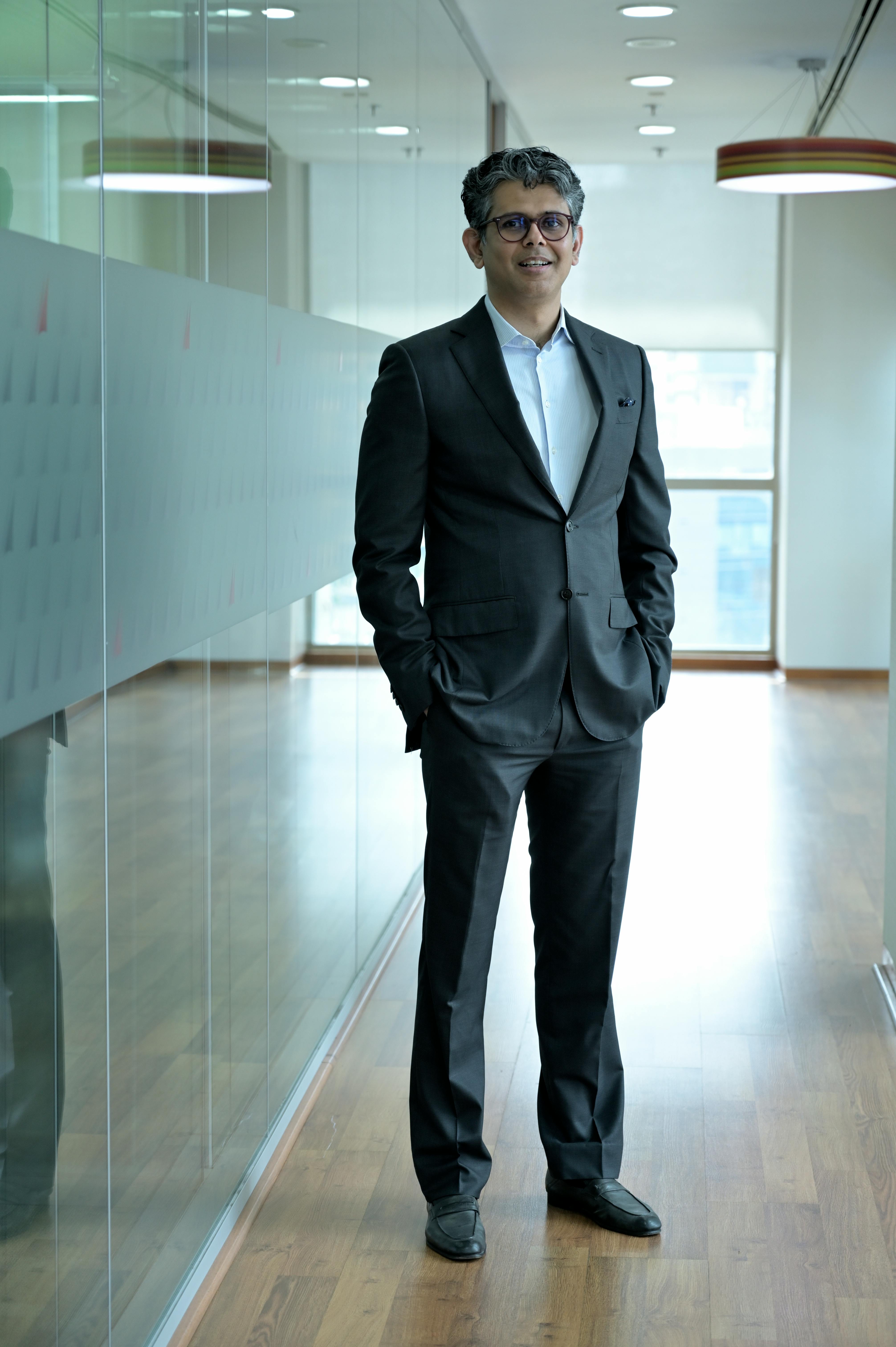Smiling businessman in a suit standing confidently in a modern office hallway.