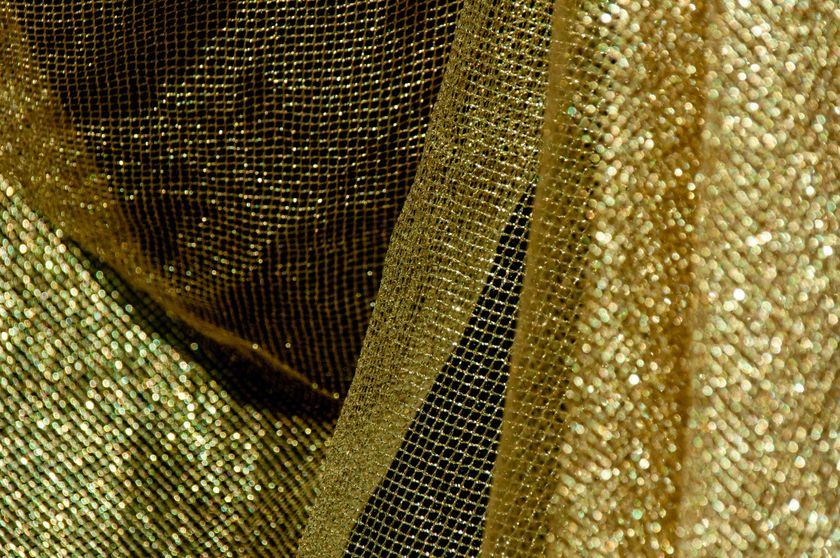 Close-up of a gold mesh cloth, the metallic yarn catching the light in points across the open weave.