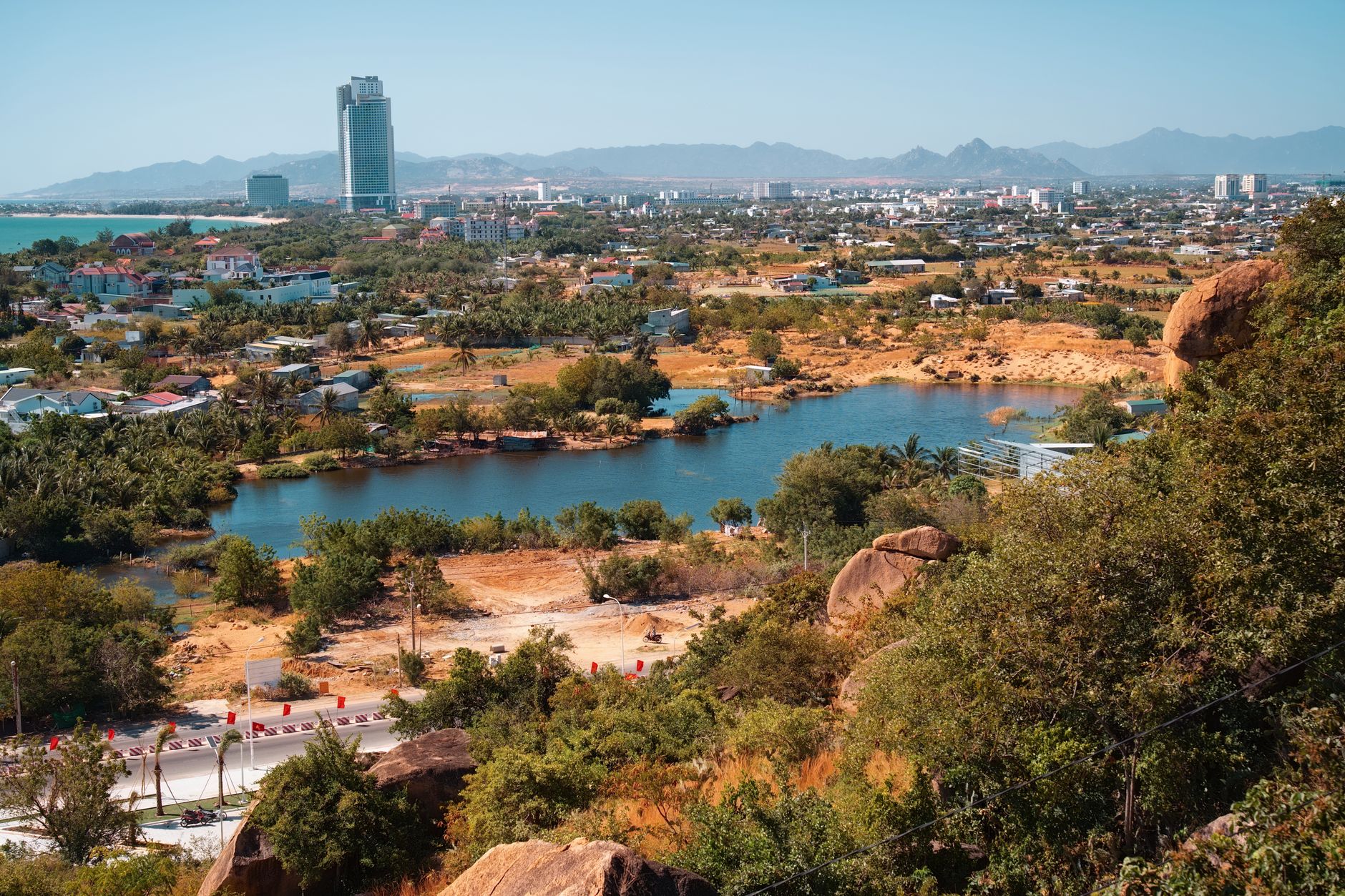 Aerial view of a vibrant cityscape with a lake and mountains, captured during a sunny summer day.