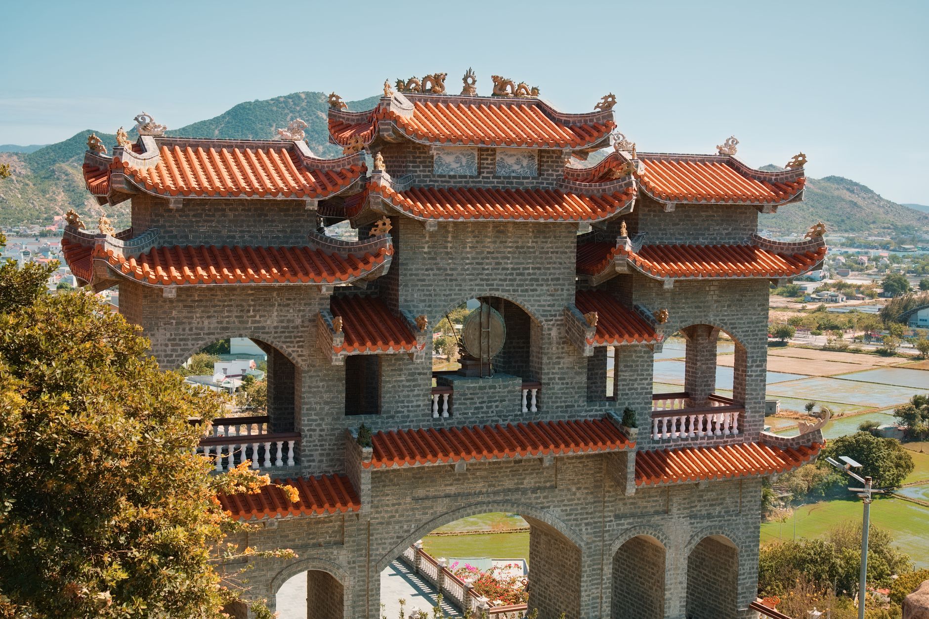 A classic Asian pagoda with vibrant red roofs set against picturesque hills and rice fields, showcasing a stunning cultural heritage site.