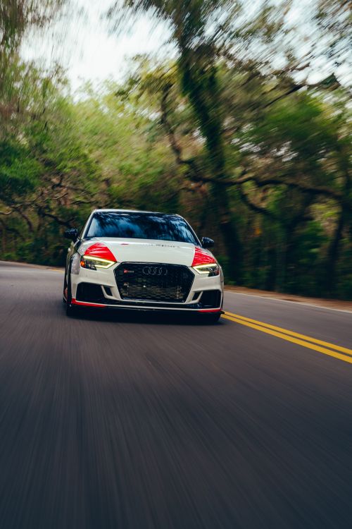 Free High-speed car driving on a curved forest road, showcasing motion blur and vibrant trees. Stock Photo