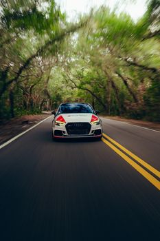 Dynamic shot of a sleek car driving through a lush forest road, highlighting speed and nature.